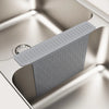 A silicone sink protector mat with drainage holes is shown in a close-up view inside a stainless steel kitchen sink.