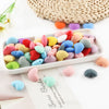 A collection of ten colorful silicone heart beads in various shades are displayed on a white tray.