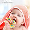 A baby is shown biting an insect-themed suction cup toy while wearing a pink towel.