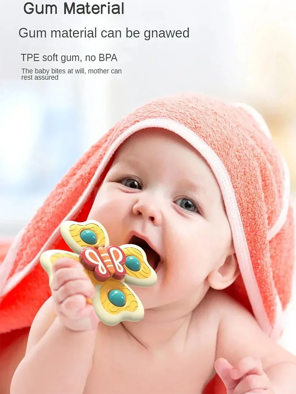 A baby is shown biting an insect-themed suction cup toy while wearing a pink towel.