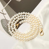 A strand of creamy white pearls on a gold chain strap for a handbag or purse.