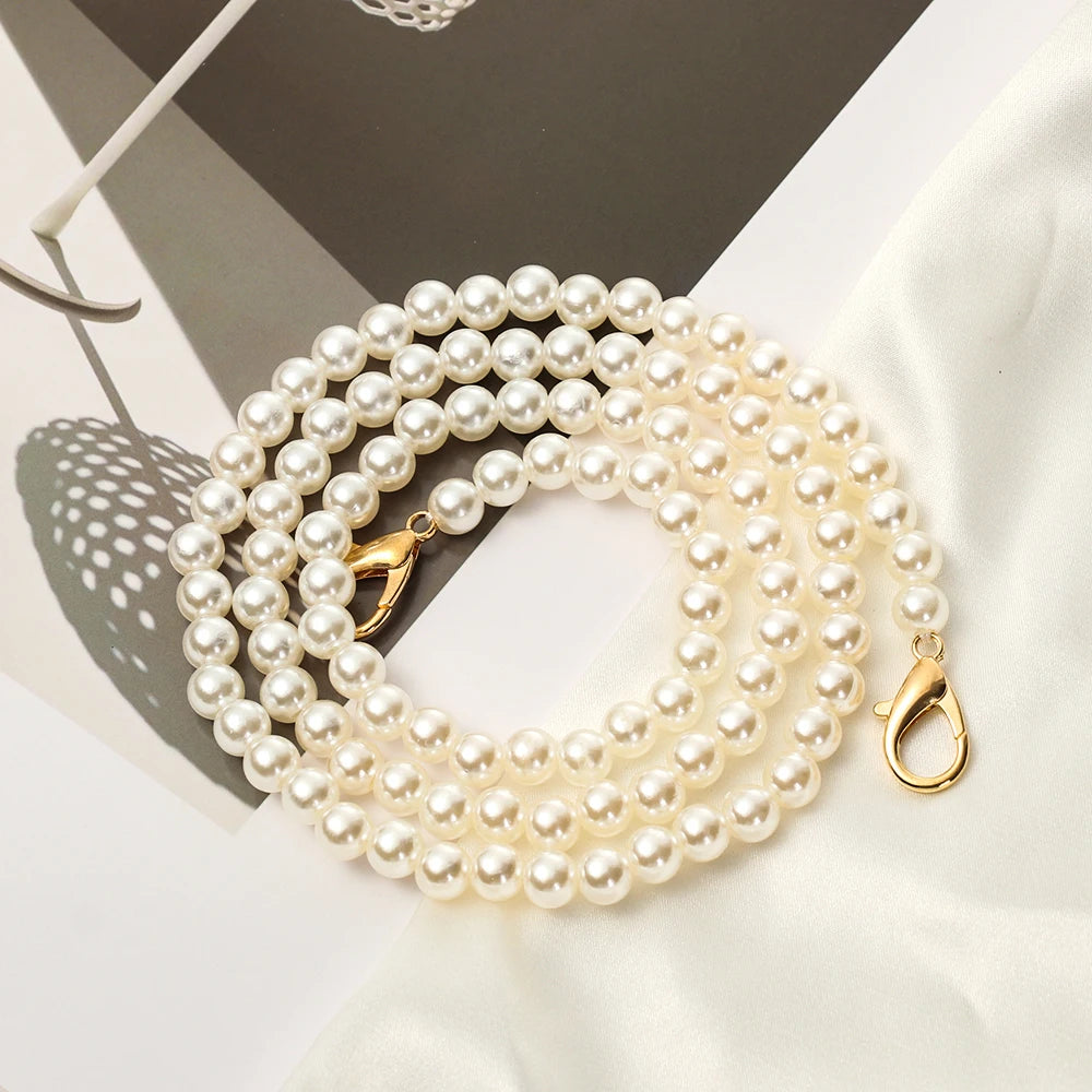 A strand of creamy white pearls on a gold chain strap for a handbag or purse.