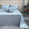 A light blue luxury bamboo flat sheet is draped over a bed with white pillows and a modern headboard.