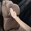 A hand is touching a brown memory foam car lumbar support and neck pillow set.