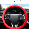 A red silicone steering wheel cover is displayed inside a car's interior, showing the steering wheel and dashboard controls.