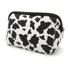 A black and white cow print cosmetic bag with a zipper, designed for travel makeup organization.
