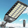A solar-powered LED security flood light with a motion sensor and remote control mounted on a pole against a blue sky.
