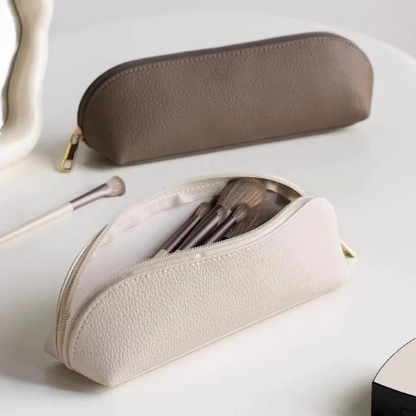 Estuche de maquillaje y lápices beige con cremallera, tumbado sobre una superficie blanca.