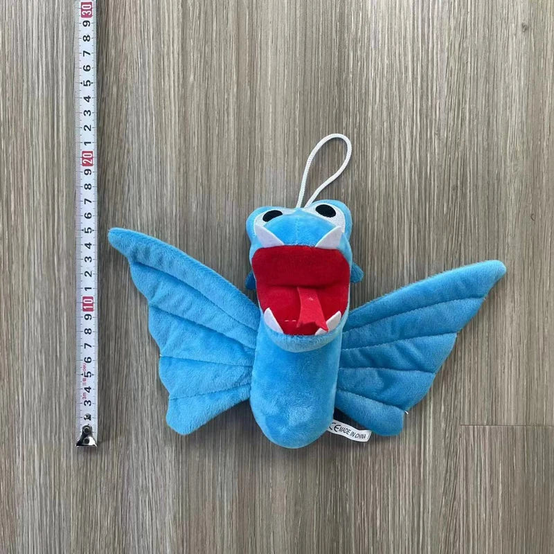 A blue plush toy of an Opila bird with large wings and a red mouth, measured against a ruler.