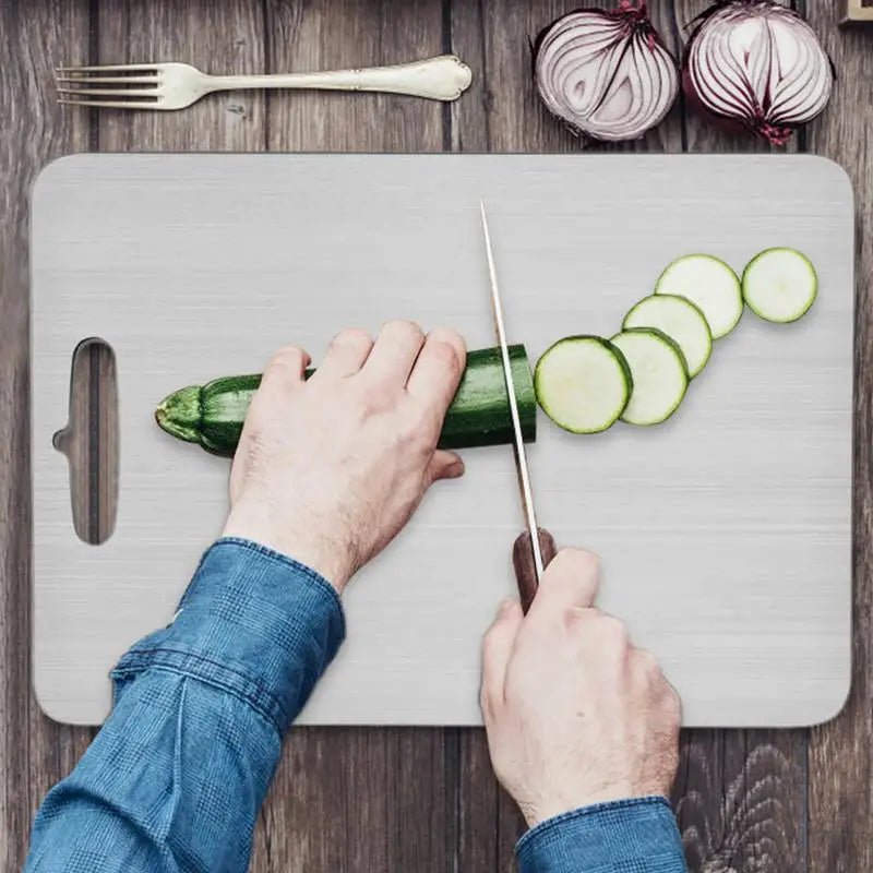 A person is cutting a cucumber on a gray cutting board with a knife, surrounded by garlic and a fork.