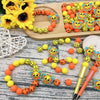 A collection of colorful 3D bee silicone beads and yellow flowers arranged on a wooden board.