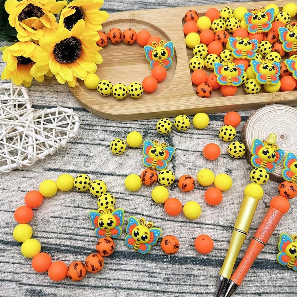 A collection of colorful 3D bee silicone beads and yellow flowers arranged on a wooden board.