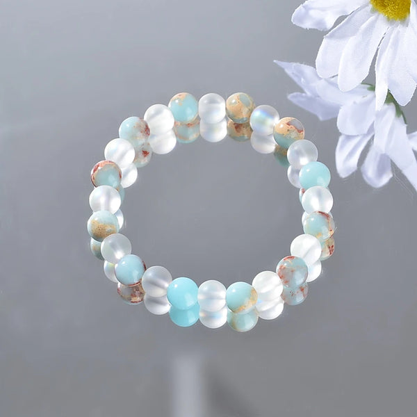 Bracelet en perles de quartz bleu clair et blanc avec inclusions naturelles, exposé à côté d'une fleur blanche