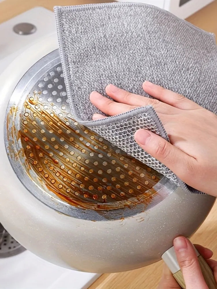 A hand is using a gray steel wire scrubber dishcloth to clean a round, silver dish.