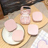 A pink compact contact lens travel case is shown open and closed on a wooden surface.