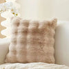 A fluffy beige faux fur decorative pillow resting on a white surface.