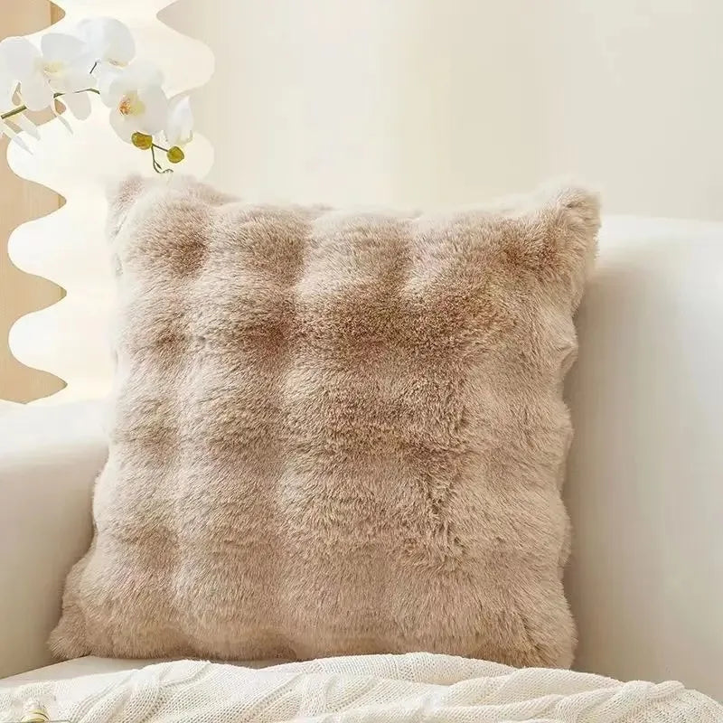 A fluffy beige faux fur decorative pillow resting on a white surface.