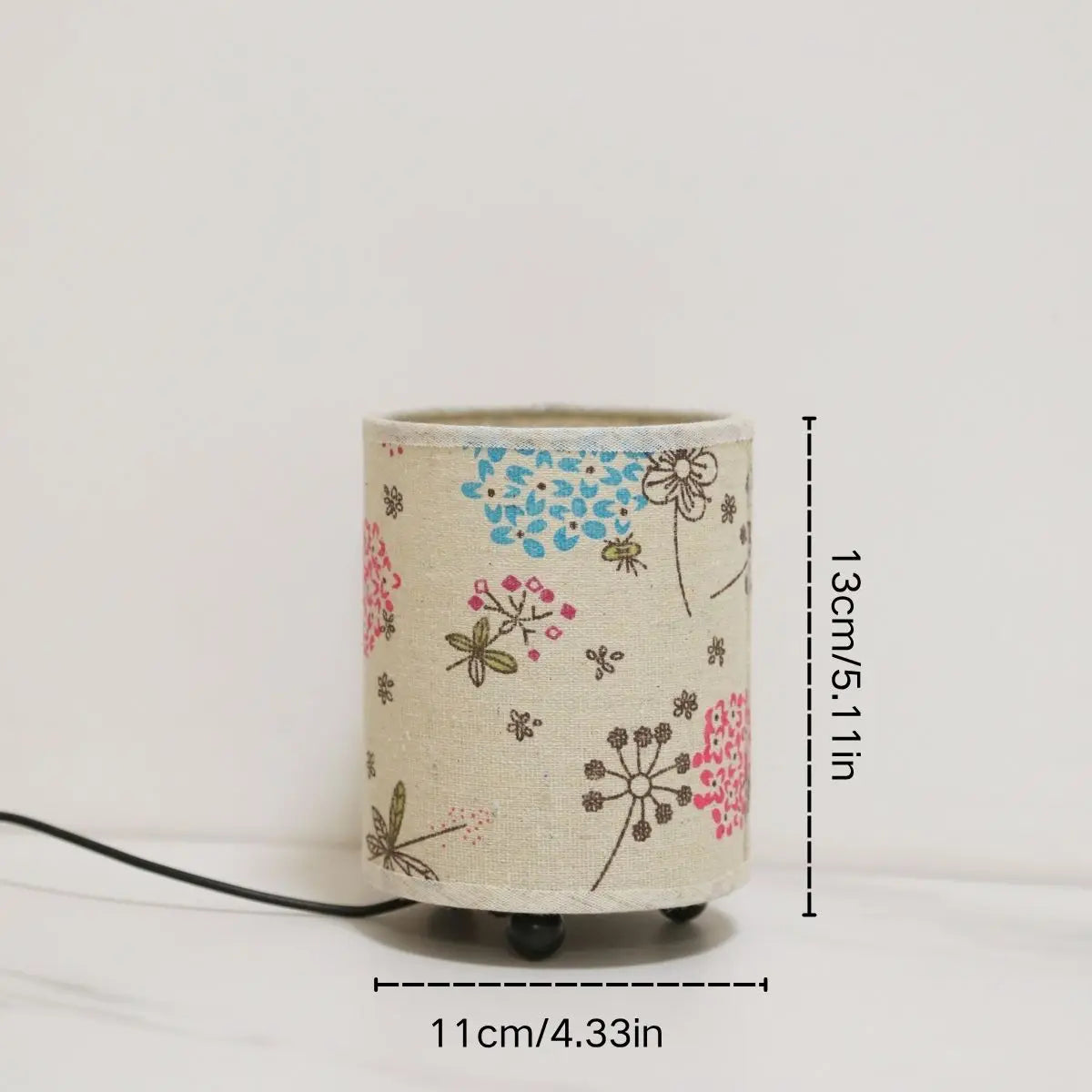 A cylindrical printed fabric desk lamp with a light beige background featuring floral patterns and a black cord.