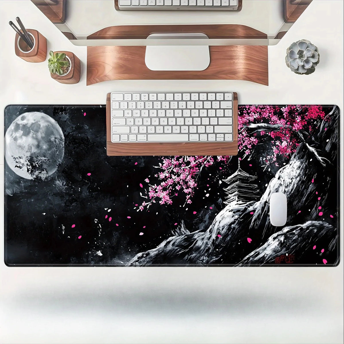 Un tapis de souris noir avec une lune, des fleurs de cerisier roses et un paysage de montagne blanche avec un clavier en bois