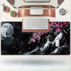 Un tapis de souris noir avec une lune, des fleurs de cerisier roses et un paysage de montagne blanche avec un clavier en bois