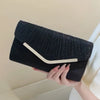 Black pleated glitter envelope clutch with a light colored strap being held by a hand.