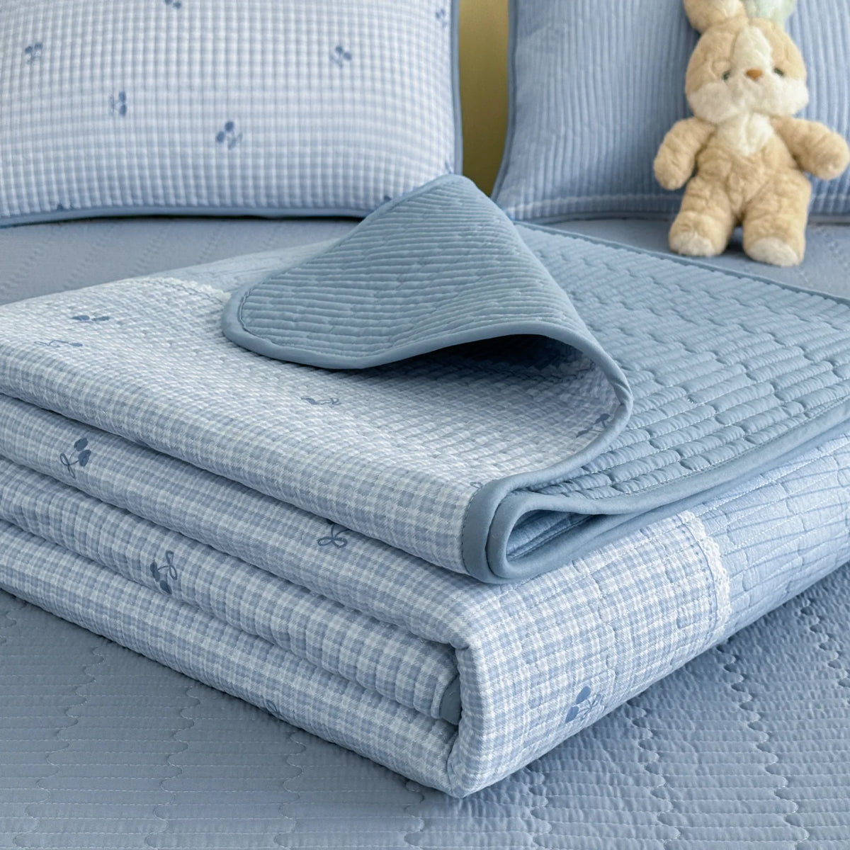 Light blue quilted bedspread and matching pillow with a small teddy bear toy