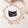 A gold chain accessory featuring starfish and pearl charms surrounding a black leather pouch.