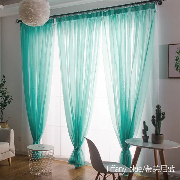Light aqua sheer voile curtains with rod pockets hanging in a bright room.
