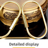 A set of gold brass keychain charms with locking carabiner clips displayed on a dark surface.
