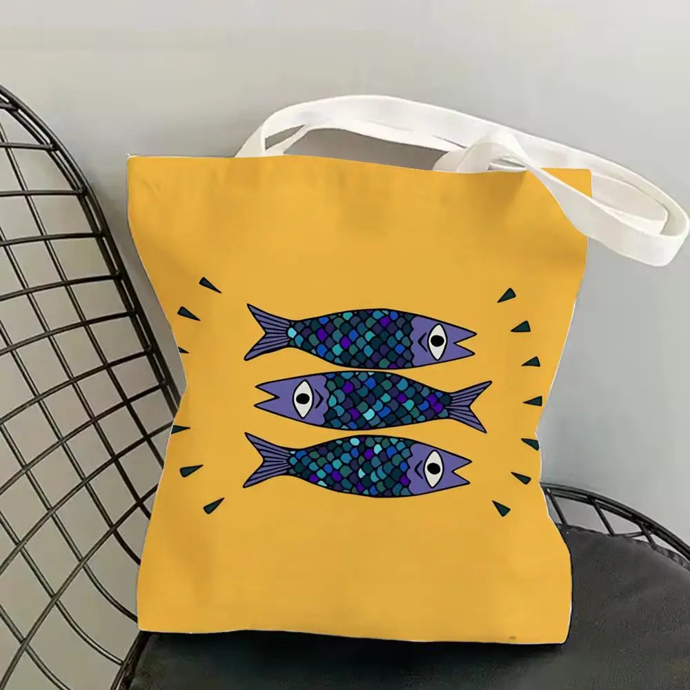 A yellow canvas tote bag featuring a print of blue and purple sardines.