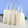 Four natural canvas shopping tote bags hanging against a light blue background.