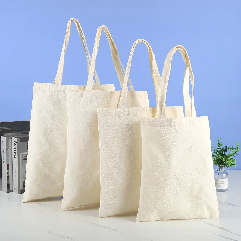 Four natural canvas shopping tote bags hanging against a light blue background.