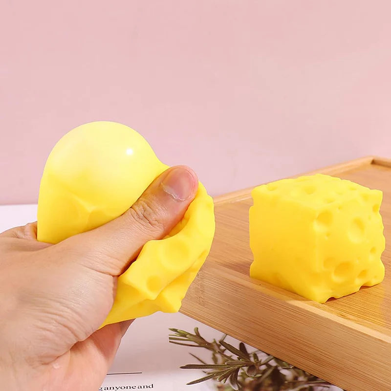 Une main serre un jouet anti-stress en forme de fromage jaune sur une planche en bois.