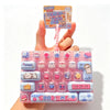 A pink plastic case filled with various colorful cartoon keycap fidget items and a small instruction card is held by a hand.