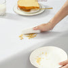 A hand is using a white cloth to wipe food residue from a plate on a table.