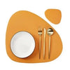 A set of orange reversible non-slip placemats with a white plate and silverware on a wooden surface.