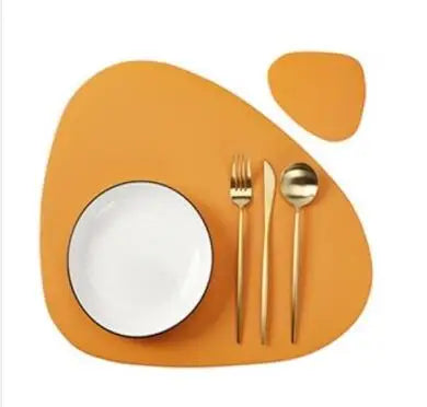 A set of orange reversible non-slip placemats with a white plate and silverware on a wooden surface.