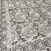 White lace tablecloth featuring an embroidered rose pattern on a wooden surface.