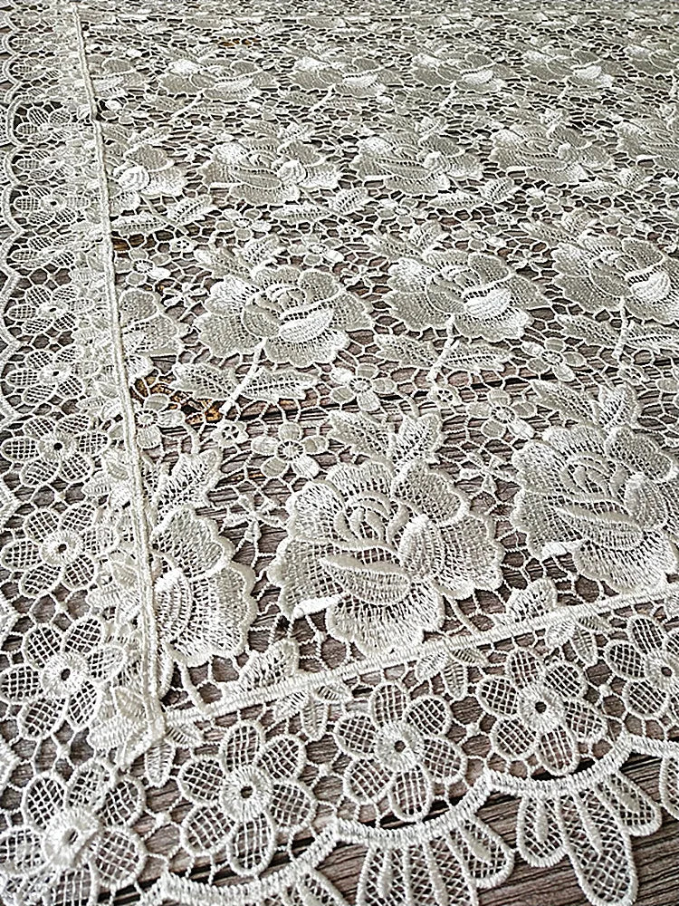 White lace tablecloth featuring an embroidered rose pattern on a wooden surface.