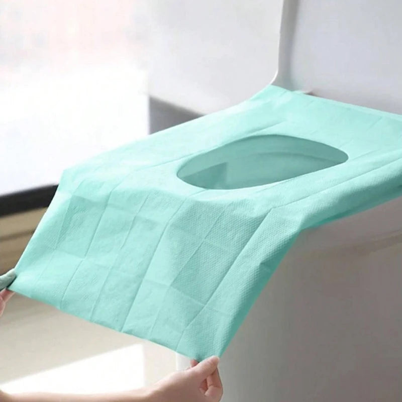 A light mint green disposable toilet seat cover is shown being placed on a white surface.