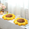 A collection of yellow sunflower-shaped pillows arranged on a white cloth with pink flowers and a cup in the background.
