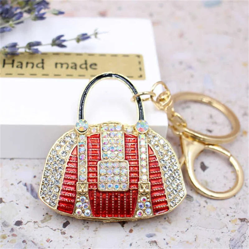 A red and white crystal rhinestone handbag keychain is displayed next to a gold-colored ring on a light surface.