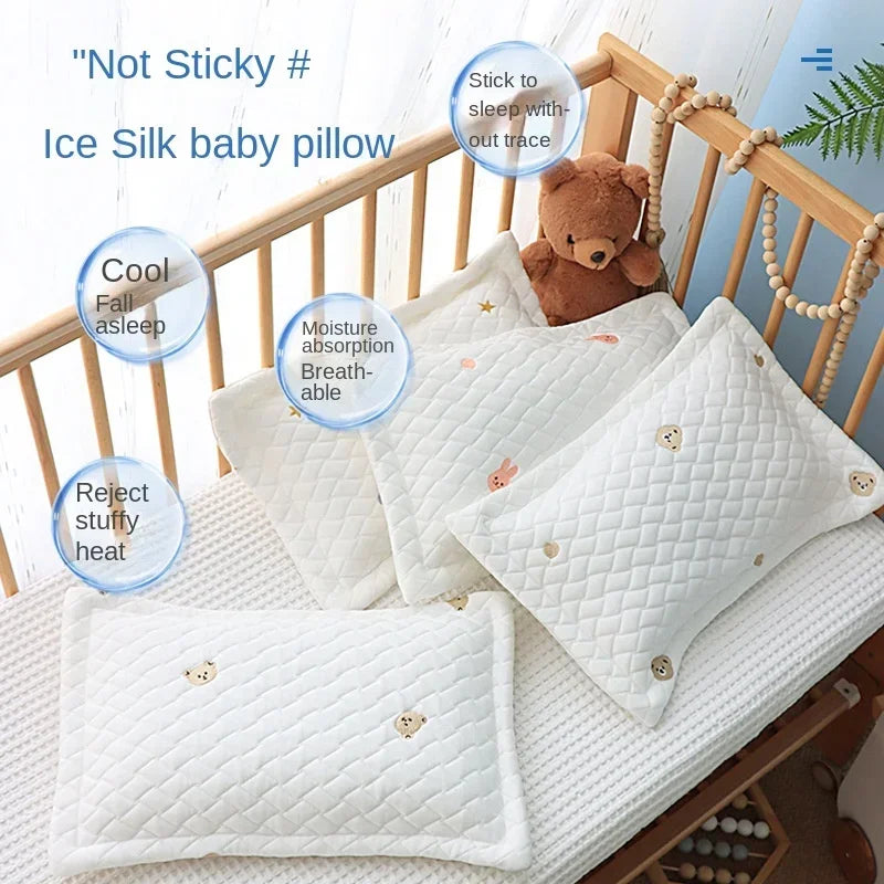 White ice silk baby pillow with a brown teddy bear toy shown in a wooden crib setting.