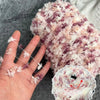 A hand is holding a ball of hand-dyed variegated yarn with pink and purple tones for knitting or crochet.