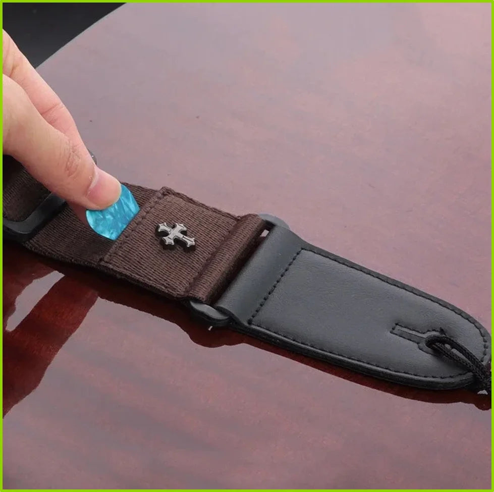 A dark brown guitar strap with a vintage cross pattern and a black pick pocket is shown being held by a hand.