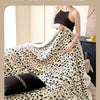A woman is wrapped in a fluffy leopard print throw blanket indoors.