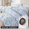 A light blue duvet cover set with a white heart print and matching pillowcases is displayed next to a white washing machine.