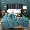 A luxury white goose and duck down comforter with a cotton cover displayed on a bed against a teal wall.