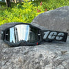 A pair of black motocross goggles with a gray strap resting on a large gray rock.