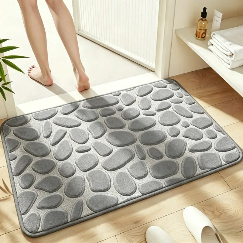 A gray plush non-slip absorbent bathroom rug with a pebble texture placed on a wooden floor.